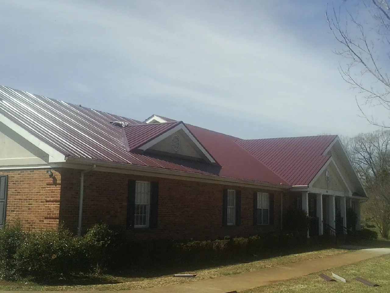 Red metal roof with gabled entries on a long brick building, from a Hail Damage Roof Repair job in Huson
