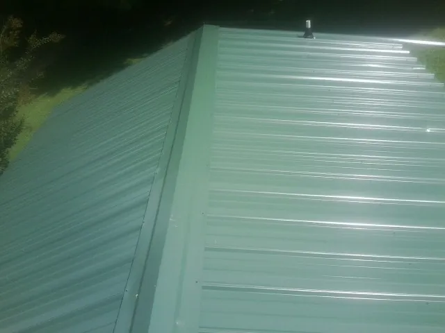 New green metal panels meeting at the ridge of a roof — Flat Roof Repair work by our crew in Huson