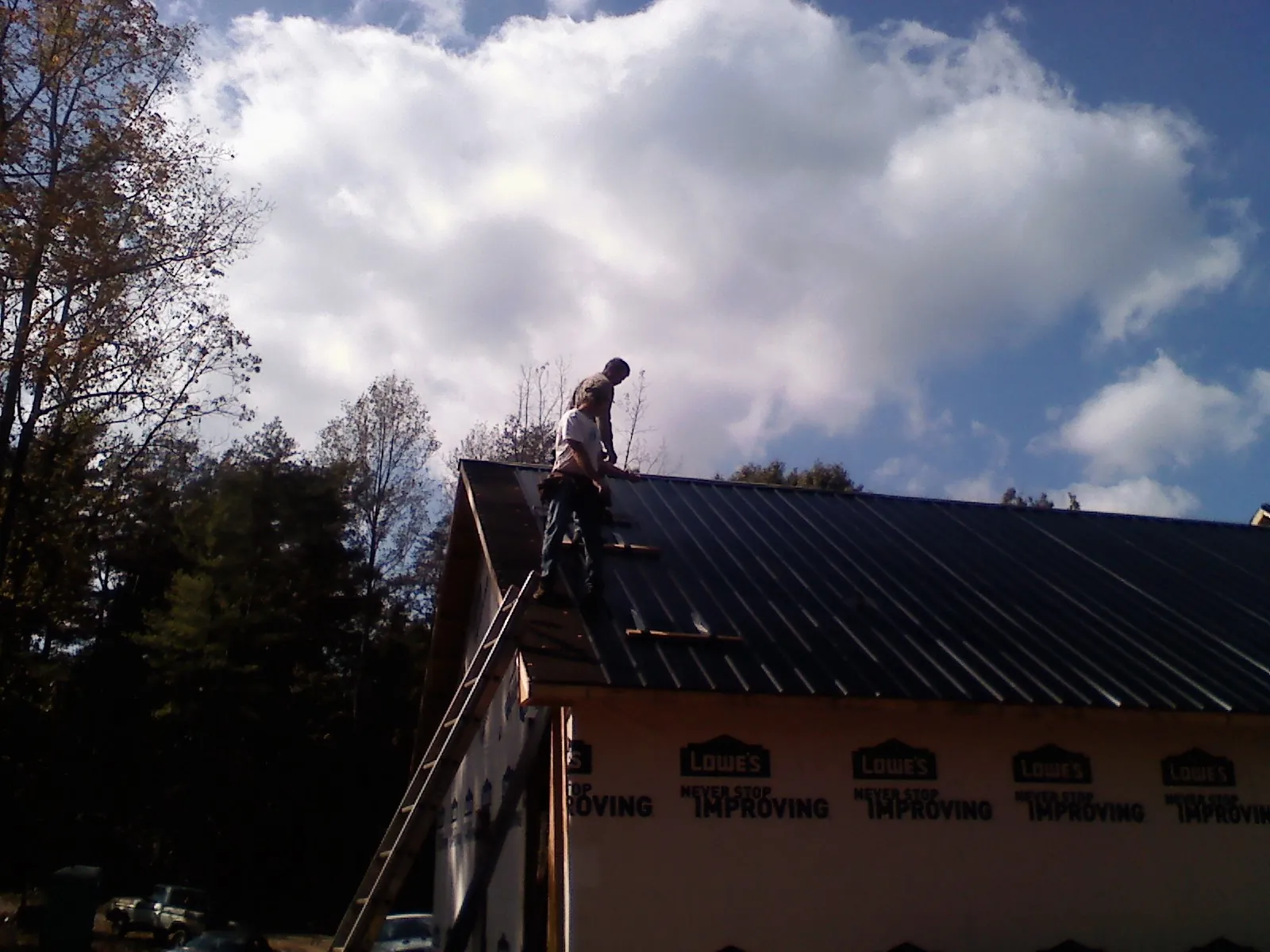 Roofer fastening dark metal panels high against a cloudy sky, from a Roof Inspection job in Huson
